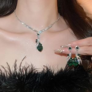 Close-up of a silver jewelry set featuring green heart-shaped gems and diamond accents