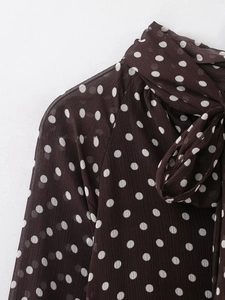 Dettaglio di una camicetta marrone scuro a pois bianchi con elegante fiocco in nastro