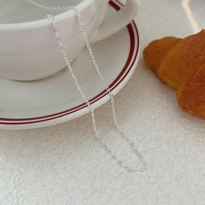 Minimalist 925 sterling silver chain necklace draped over a white ceramic teacup