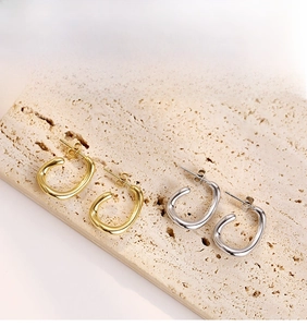 Detailed view of irregular U-shaped gold and silver earrings on a beige stone surface