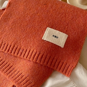 Detail of orange knit scarf featuring soft ribbed texture and decorative 'emo' label