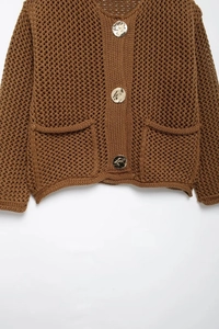 Détail du cardigan en maille marron chaud montrant le tissage et les boutons en métal doré