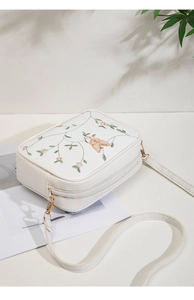 Detail of white camera bag featuring floral embroidery and a 3D pink butterfly decor