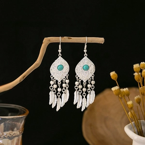 Detail of silver Bohemian tassel earrings with turquoise stones on a dark wood branch