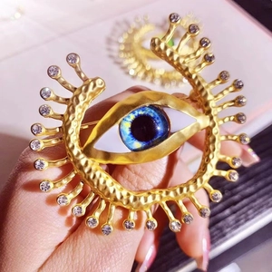 Detailed close-up of golden metal evil eye brooch with blue stones and sparkling crystals