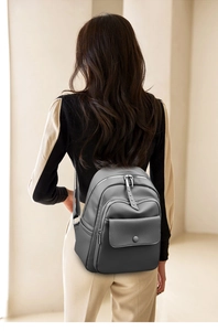 Gray leather backpack with multiple zip pockets shown on a model from the back view