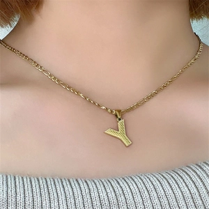 Primo piano di una collana dorata con ciondolo lettera Y e catena Figaro su modella