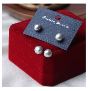 Macro shot of grey freshwater pearl earrings set on black jewelry card and red velvet box