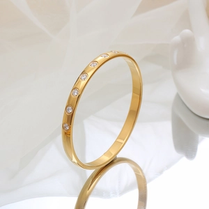 Polished gold titanium steel bangle with embedded diamonds on elegant white silk backdrop