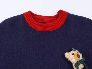 Detail of navy knit sweater featuring a red ribbed neck and cute plush bear accessory