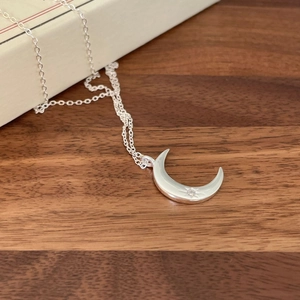 Macro view of polished silver moon pendant with a sparkling zircon on dark wood