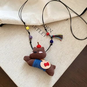 Close-up of fabric bear pendant with blue overalls and colorful beads on a beige book