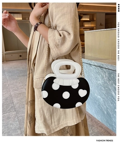 Close-up of black and white heart-patterned handbag with golden chain strap on model