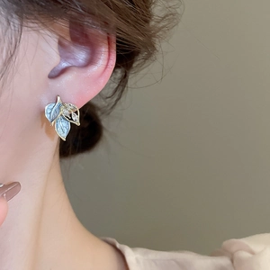 Detail of leaf-shaped earrings with light blue enamel and zircon worn by a model