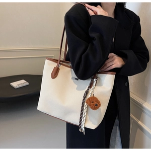 Detail view of cream canvas tote bag with brown leather trim and cute teddy bear pendant