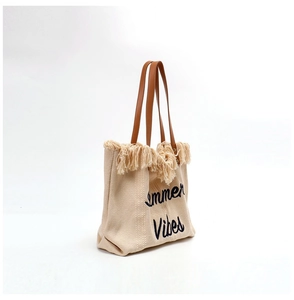 Detail of beige woven tote bag with fringe edge and Summer Vibes embroidery