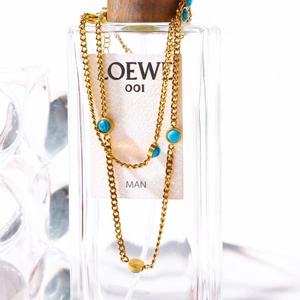 Gold chain necklace with blue turquoise stones draped over a clear perfume bottle