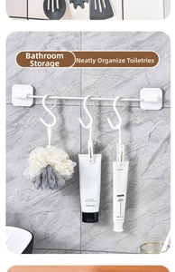 Close-up of a white wall-mounted storage rod with S-hooks and clips on marble tile