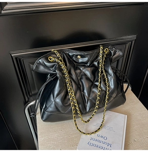 Detail of black quilted leather bucket bag with gold-tone chain strap on stone surface