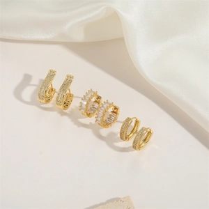 Three pairs of elegant gold hoop earrings with zircon stones on white silk fabric