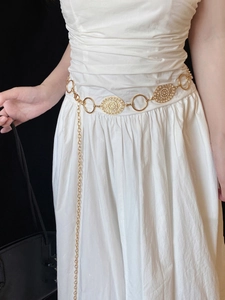 Detailed view of a vintage gold waist chain with hollow patterns and pearl accents on white dress