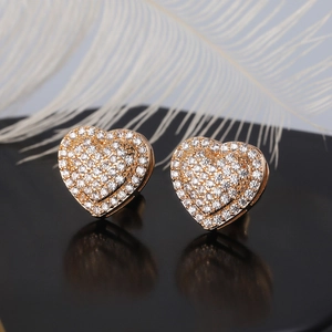 Detail of gold heart earrings with micro-set zircons on a black mirror with feathers