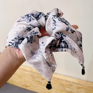 Detailed view of beige floral pattern hair scrunchie with small black tassel charms