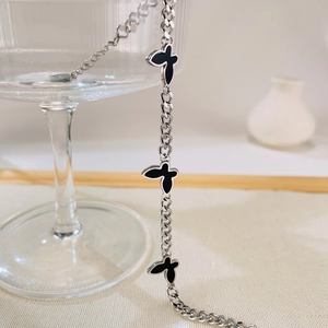 Detail of silver chain bracelet with black acrylic butterfly charms on a glass
