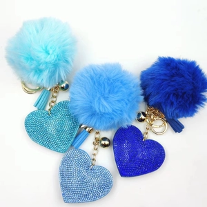 Detail of three blue rhinestone heart keychains with matching faux fur pom poms and tassels