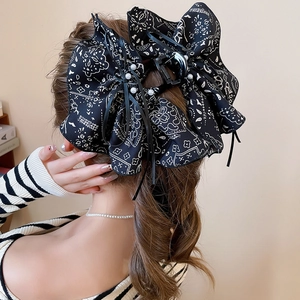 Detail view of large black bow hair claw with floral print and pearls worn on hair