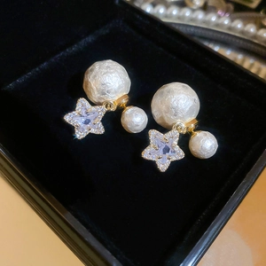 Close-up of star-shaped zircon earrings with textured pearls on black velvet