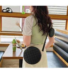 Model wearing a black round quilted crossbody bag with a small matching coin purse attachment