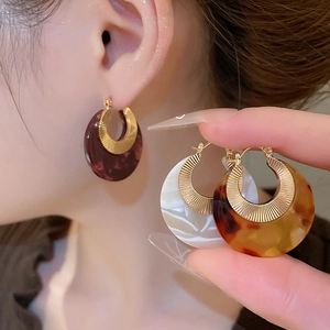 Close-up of acetic resin C-shaped hoop earrings with gold metal accents and tortoiseshell texture