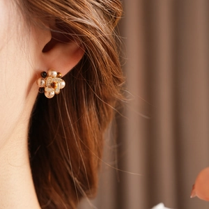 Detailed view of flower earrings with pearls and amber stone on model's ear
