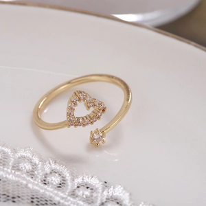 Adjustable gold heart ring with pavé zircon stones on white ceramic and lace background