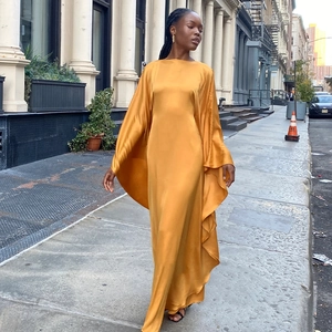 Elegant gold satin kaftan maxi dress with batwing sleeves flowing in an urban street setting