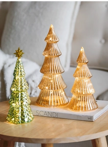 Glow from glass Christmas trees with LED lights and gold stars on a wooden table