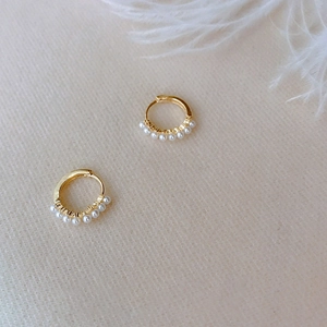 Detailed view of gold hoop earrings with small white pearls on a soft fabric background