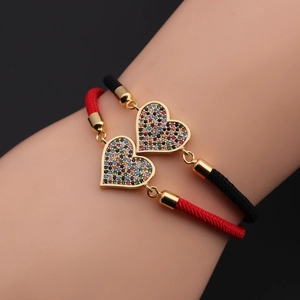 Detail of hand-woven couple bracelets featuring gold heart charms with colorful cubic zirconia