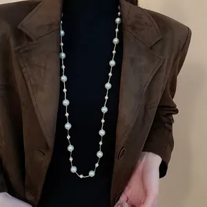 Long station necklace with white artificial pearls on a gold chain worn over a brown blazer