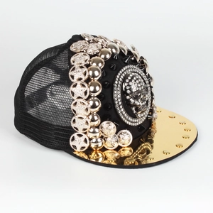 Detail of a punk style trucker hat with golden visor, metal studs and a large skull ornament