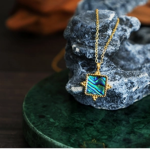 Detailed close-up of square abalone shell pendant on a 18K gold-plated chain necklace