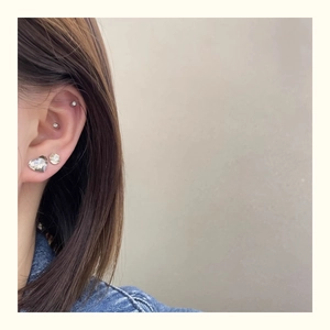 Close-up of heart and round crystal stud earrings on ear with silver cartilage jewelry