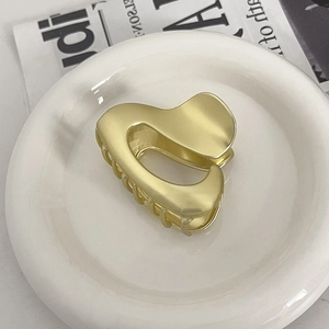 Detailed view of a matte gold heart-shaped metal hair claw clip on a white plate