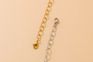 Detail of gold and silver necklace extenders with lobster clasps on a peach background