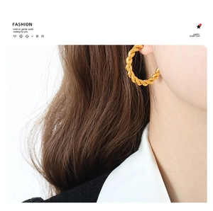 Close-up of model wearing chunky twisted gold hoop earrings in a minimalist style