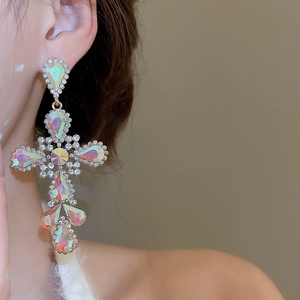 Close-up of dangling cross earrings with colorful crystals and gold plating on model
