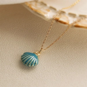 Elegant gold shell pendant necklace with blue enamel drip on a textured beige surface