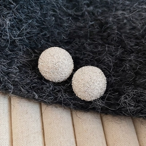 Minimalist round stud earrings with textured stardust finish for women set on grey fabric