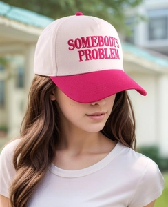 Detail of embroidered 'SOMEBODY'S PROBLEM' text on pink cotton baseball cap crown